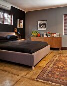 Double bed with grey upholstered frame and black bed linen in dark-painted master bedroom