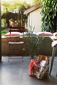 Shopping basket on terrace floor and simple metal folding chair in front of parapet wall with striped cushions and palm trees in courtyard