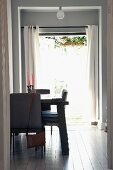 Essplatz mit rustikalem Tisch im Gegenlicht einer offenen Fenstertür zum Garten