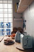 Vintage-style toaster and kettle on kitchen worksurface in front of window with view of maritime anchor motif