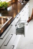 Kitchen counter with dark stone worksurface and set of white dishes in open drawer