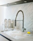 Kitchen counter with pale grey marble worksurface and splashback, flexible spray tap fitting and foaming water in sink