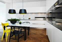 weiße Einbauküche mit Marmorplatten für Arbeitsbereich und Esstisch, Stühle in Gelb und Schwarz