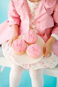 A girl dressed in pink holding a plate of pink cupcakes