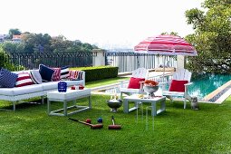 White outdoor furniture with red, white and blue accessories in front of pool; croquet set in foreground on lawn in luxurious gardens