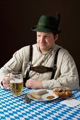 A stereotypical German man wearing lederhosen and eating white sausage with a beer