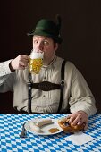 A stereotypical German man wearing lederhosen and eating white sausage with a beer