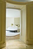 Wood-panelled, traditional doorway leading to elegant bedroom with designer furniture in pastel-grey colour scheme