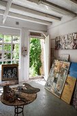 Artist's studio - painting utensils on table and pictures leaning against wall next to open door with view into garden