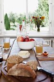 Gedeckter Holztisch mit Vollkornbrot, Brötchen, Butter, Obst und Apfelsaft