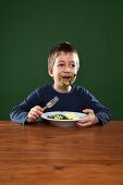 Mit Spinat verschmierter Junge isst Spinat mit Kartoffeln