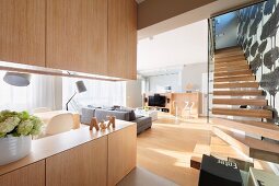 Ober- und Unterschrank aus hellem Holz als Raumteiler in offenem, modernem Wohnraum, seitlich Treppenaufgang mit Massivholzstufen
