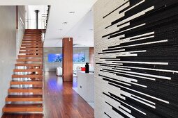 Treppenaufgang mit Massivholzstufen in modernem, offenem Wohnraum, im Vordergrund Raumteiler mit schwarzen und weissen Riemchen-Fliesen