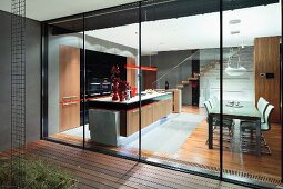 View from terrace through sliding glass wall into illuminated kitchen-dining area in contemporary house