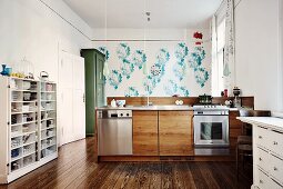 Spacious kitchen with free-standing counter below row of pendant lamps opposite white, half-height shelves against wall