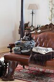 Stacked jumpers and blankets on antique bench with brown, leather upholstery and carved wooden frame in rustic, traditional bedroom