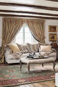 Ottoman with curved legs on Oriental rug, sofa below lattice window with draped curtains