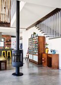 Free-standing wood-burning stove on concrete floor, sideboard and vintage shelving unit against staircase in open-plan interior