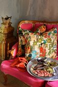 Vorspeisen auf Silberplatte vor Kissen mit folkloristischem Motiv, auf pinkfarbener Sitzbank