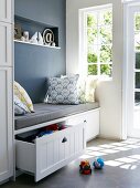 Bench with grey seat cushion, scatter cushions and drawers for storing toys in niche next to window
