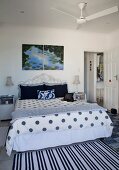 Striped and polka dot patterns on bed linen and rug in rustic bedroom with ceiling fan