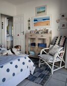 Hund auf Bett, gegenüber weisser Bambusstuhl mit Kissen, neben Kommode mit Glastüren in ländlich-maritimen Schlafzimmer