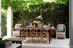 Long dining table and bentwood chairs flanked by wicker chairs on paved, summery terrace