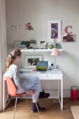 Girl using laptop on desk below floating shelf