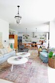 White coffee tables with amorphous tops on vintage rug in lounge area; woman in dining area of open-plan kitchen in background