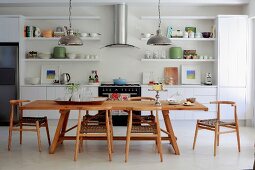 Solid wood dining table and chairs in open-plan kitchen with white fitted cabinets and open-fronted shelving