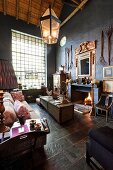 Loungebereich mit hellem Sofa und antiquarische Sammlerstücke in hohem Wohnraum mit offenem Kamin und Sprossenfenster