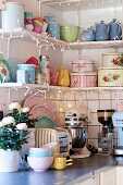 Pastel, retro crockery on shelving decorated with fairy lights above kitchen counter