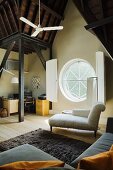 View over sofa to chaise longue in front of porthole window with interior shutters in attic room