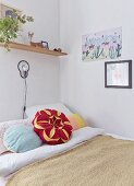 Kissen in Blütenform auf Bett, darüber Wandleuchte und Wandboard in Zimmerecke