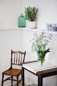 Wiesenblumenstrauss in Glasvase auf Wandtisch, seitlich antiker Holzstuhl