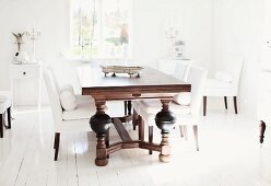 Dark, solid wood table with turned legs and elegant, white upholstered chairs on rustic wooden floor
