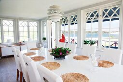 Conservatory ambiance in Swedish country house with classic, Scandinavian lamp above oval dining table with round, raffia place mats