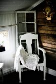 Spitzendecke auf weiss lackiertem Stuhl mit Sitzpolster in Zimmerecke, in holzverkleidetem Dachzimmer