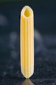 A piece of fresh penne rigate pasta on a dark marble surface