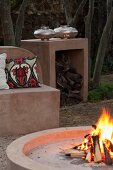 Feuerstelle mit Feuer, gemauerte Sitzbank und Beistelltisch im Garten