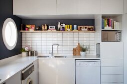 Oberschränke und dekoriertes Wandbord über Spülbecken in einer Einbauküche; seitlich Bullauge