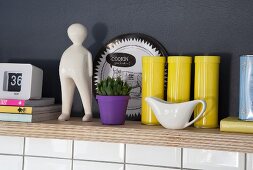 Yellow tins, purple plant pot and porcelain figurine on multiplex wooden shelf in niche
