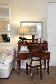 Antique chair and bureau made from dark wood, table lamp with pale lampshade and white sofa