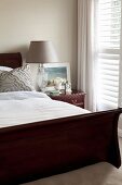 Bed with dark wooden frame and bedside lamp with pale grey lampshade in elegant bedroom