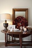 Dekorierter Holz Wandtisch mit weihnachtlichem Kranz aus roten Blättern und Windlichter, seitlich Tischleuchte mit hellem Stoffschirm