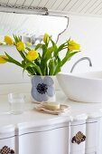 Vase of yellow tulips next to countertop basin on white washstand