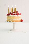 A birthday cream cake with raspberries and golden candles