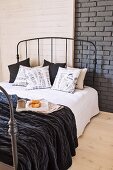 Breakfast tray on bed with dark metal frame against grey-painted brick wall partially panelled in wood