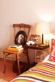 Bedside table decorated with flea market finds and pictures next to cosy mixture of patterns on bed in bedroom