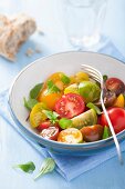 A colourful tomato salad with a chunk of bread an basil leaves
